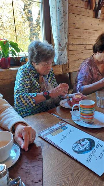 eine ältere Frau, die an einem Tisch sitzt und Essen isst